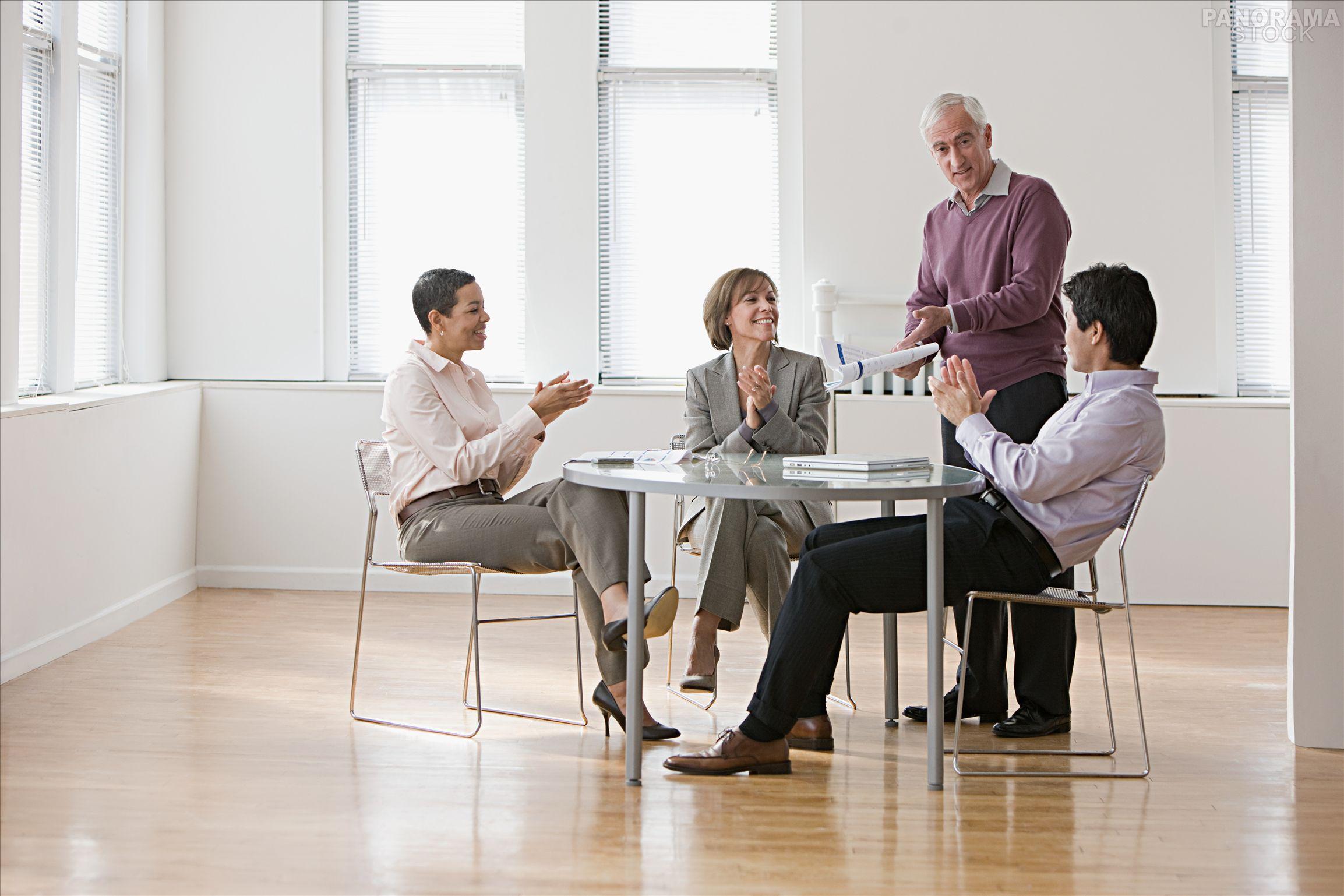 Four businesspeople at boardroom table watching presentation